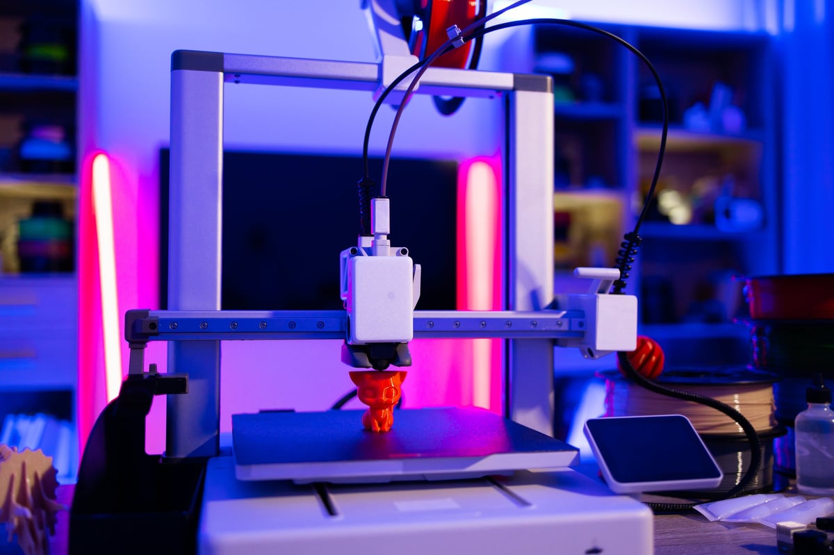 Drukarka 3D tworząca pomarańczową figurkę