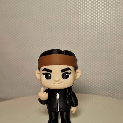 Chibi-styl figurka osoby w czarnej skórzanej kurtce i brązowej opasce na głowie, uśmiechnięta
